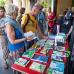 Een groep mensen staat voor het Duurzaamheidscentrum. Rechts is een rode tafel met daarop verschillende boeken met duurzame onderwerpen. Voor de tafel staan verschillende bezoekers die door boeken bladeren.